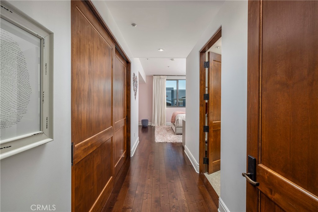 Hallway with wood doors and hardwood floors leading to a bedroom with a bed and window.