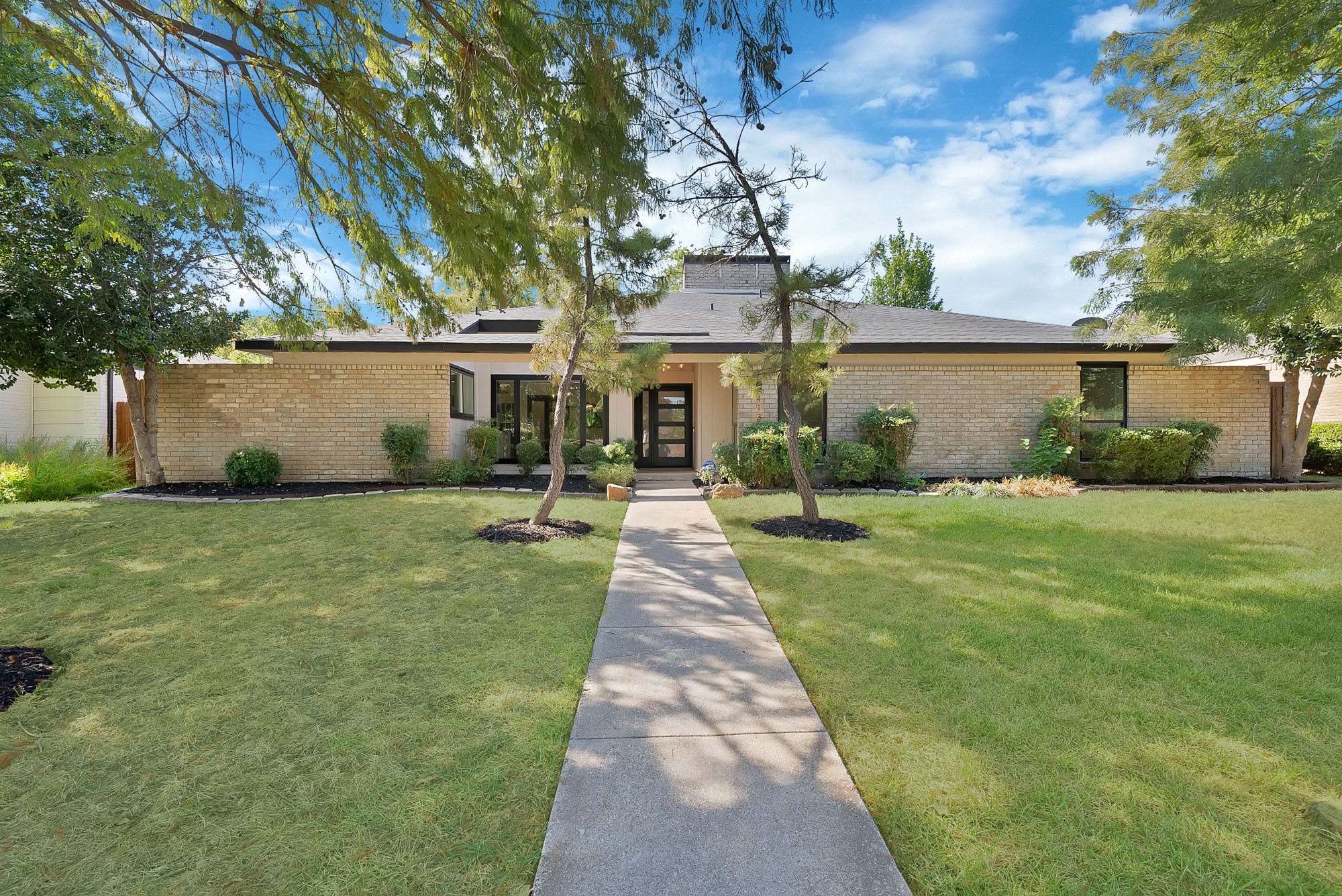 Single-story brick home with a gray roof and a walkway through a tree-shaded lawn.