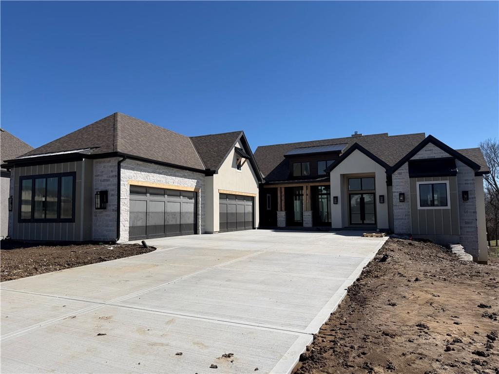 Modern stone-and-siding home with two garage doors and a broad concrete driveway.