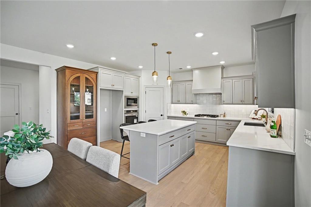 Bright kitchen with a large island, gray cabinetry, stainless steel appliances, and light wood floors.