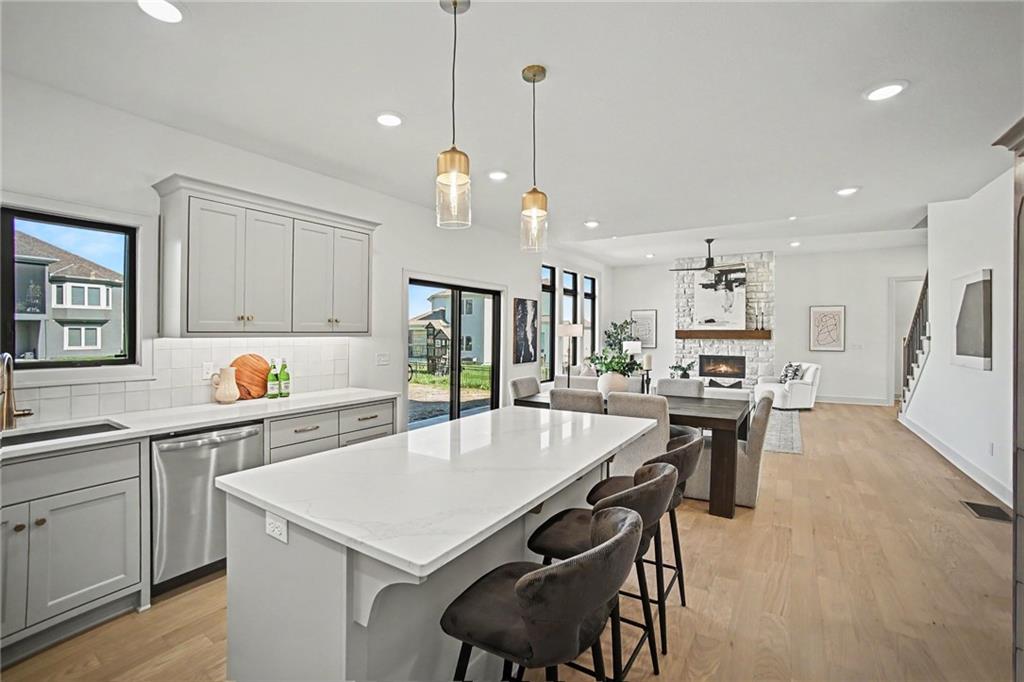 Open-plan kitchen with a large white island, dark stools, and a stone fireplace beyond.