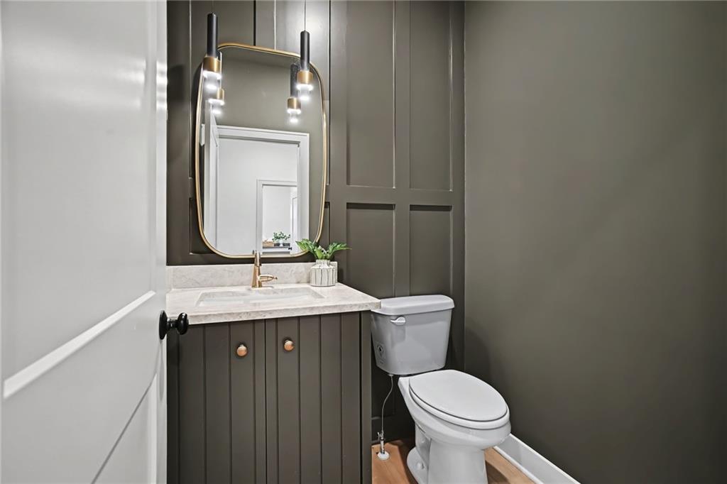 Bathroom with dark paneled vanity, marble-look counter, gold-framed mirror, and pendant lights.