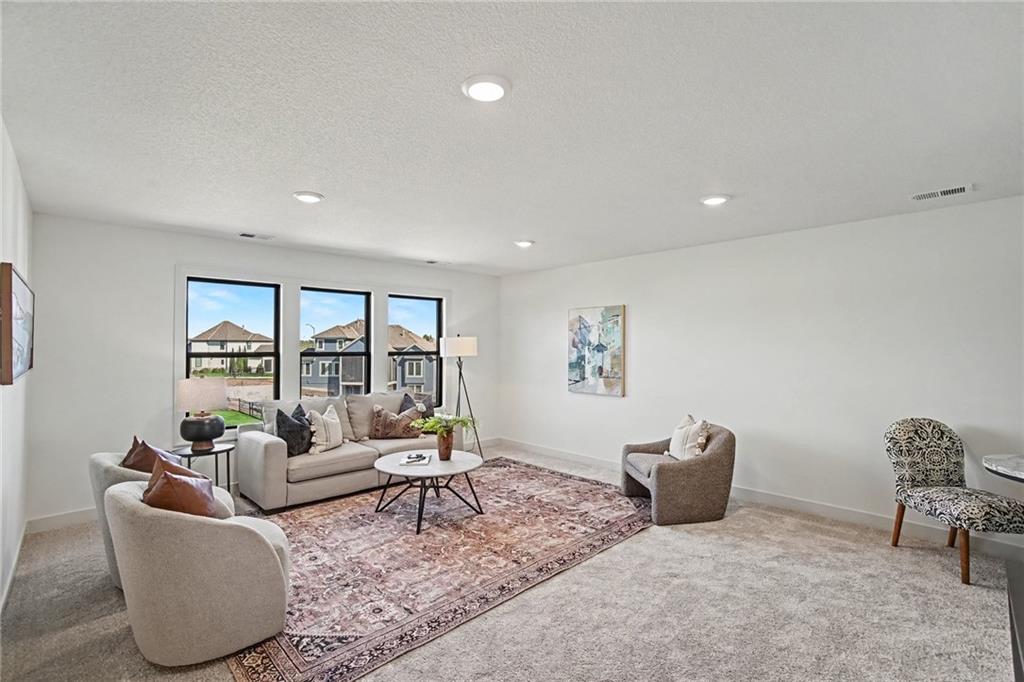 Staged living room with a beige sofa, patterned rug, and large windows overlooking neighboring houses.