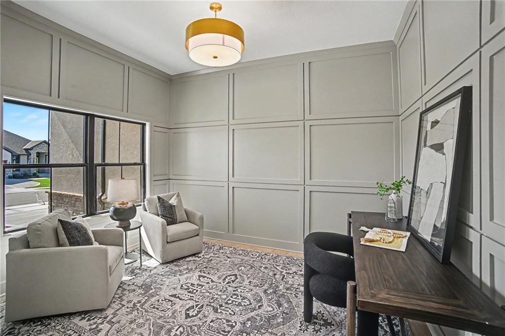 Staged sitting room with paneled gray walls, armchairs, patterned rug, and dark wood desk.