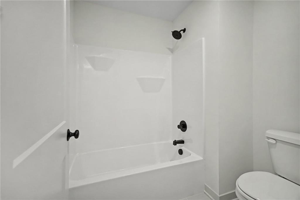 White bathtub and shower with built-in shelves and matte black fixtures beside a toilet.