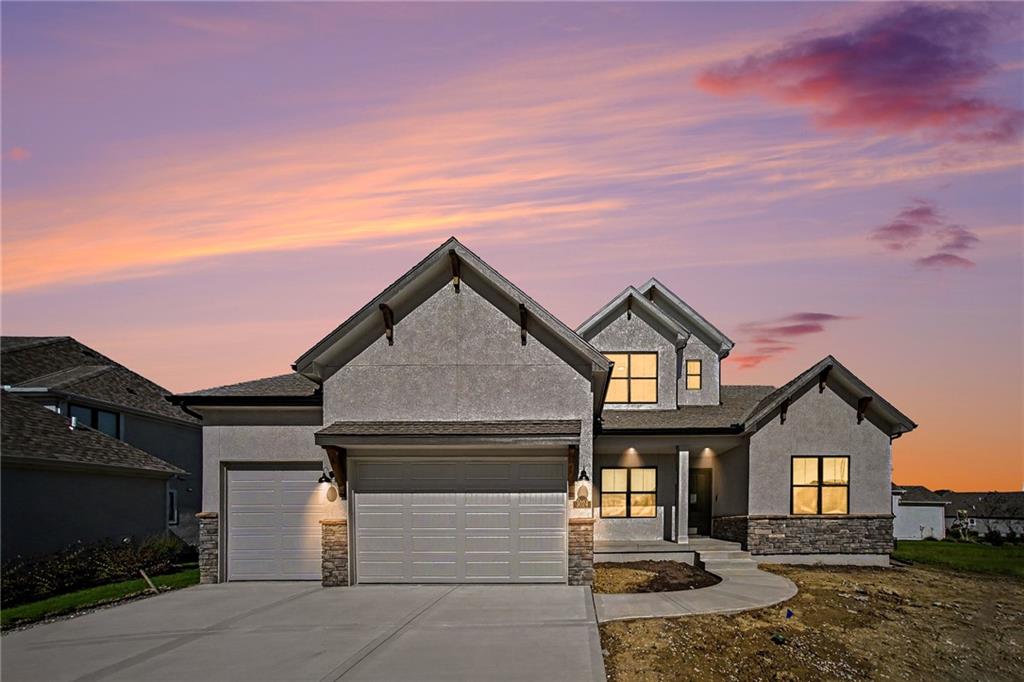 Two-story gray stucco house with stone accents and a two-car garage beneath a colorful dusk sky.
