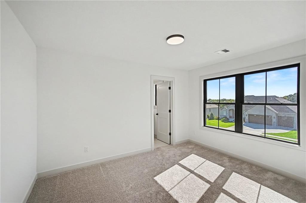 Empty carpeted bedroom with a large black-framed window overlooking neighboring homes.