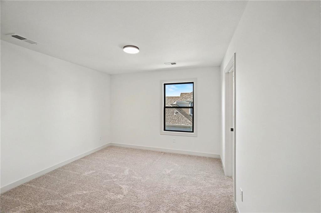 Empty carpeted bedroom with a single window overlooking neighboring rooftops.
