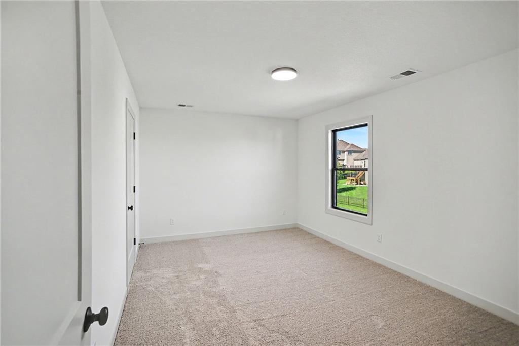 Empty carpeted bedroom with white walls and a window overlooking a green backyard.