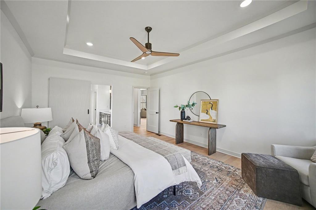 Staged bedroom with a white bed, tray ceiling, wood-blade fan, and console table.