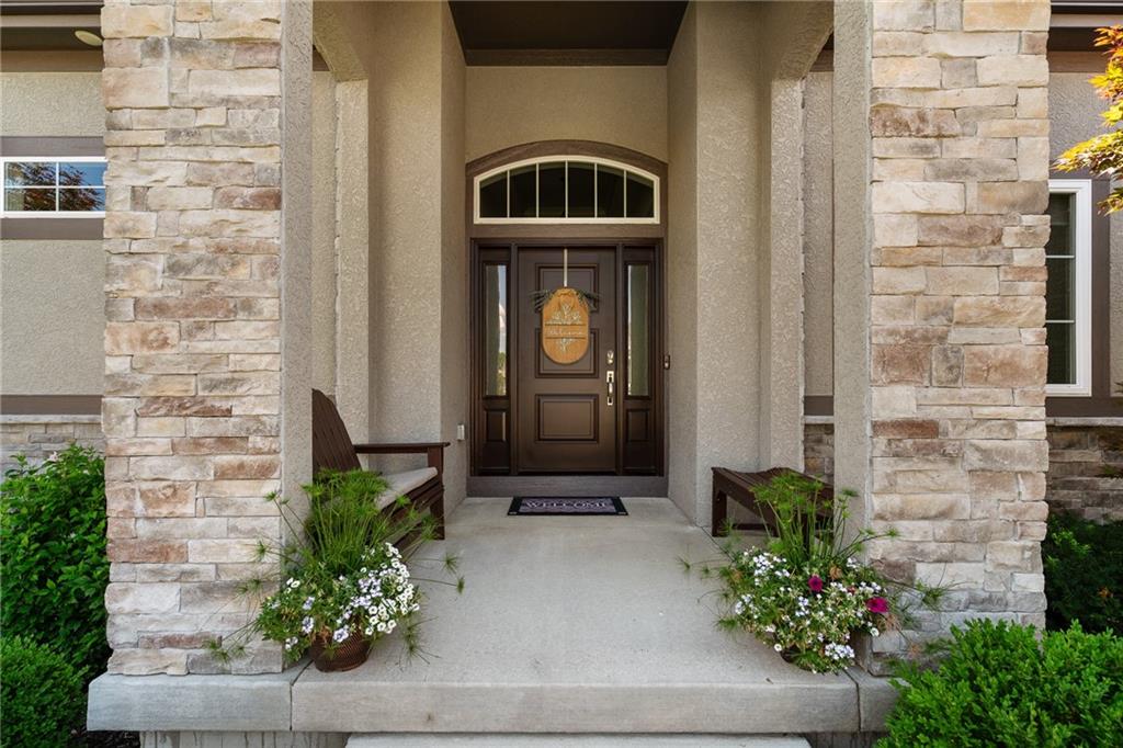 Stone home entrance with a recessed dark wood door, arched window, and flower planters.