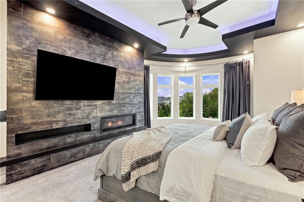 Bedroom with a stone feature wall, linear fireplace, large bed, and curved tray ceiling.