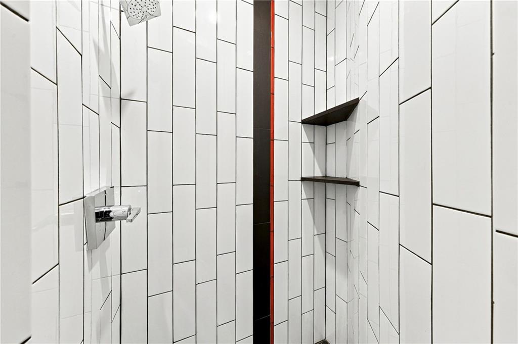 Modern tiled shower with a rainfall showerhead, built-in shelves, and a black-and-red accent stripe.