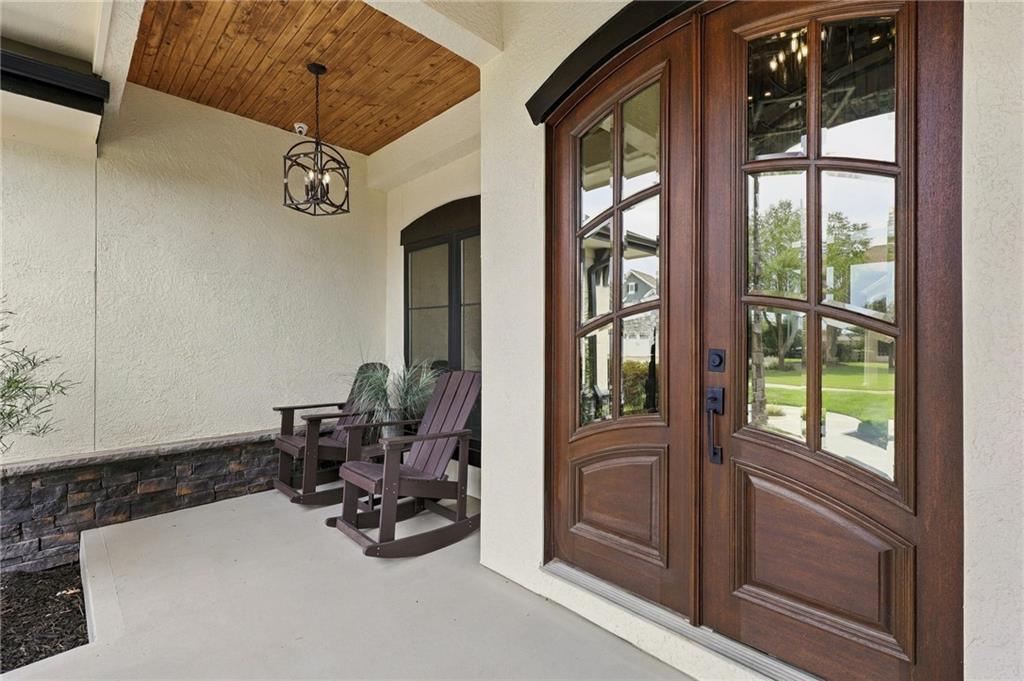 Covered front porch with a wood-plank ceiling, two rocking chairs, and a dark wood double entry door.