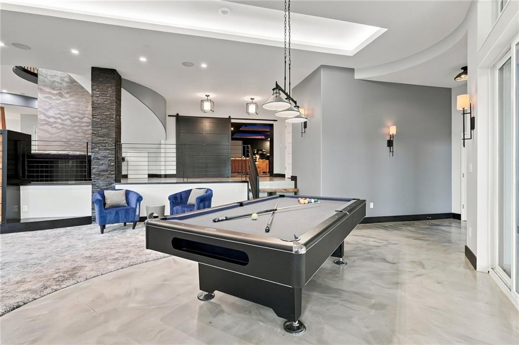 Game room with a billiards table, blue armchairs, and a modern stone fireplace.