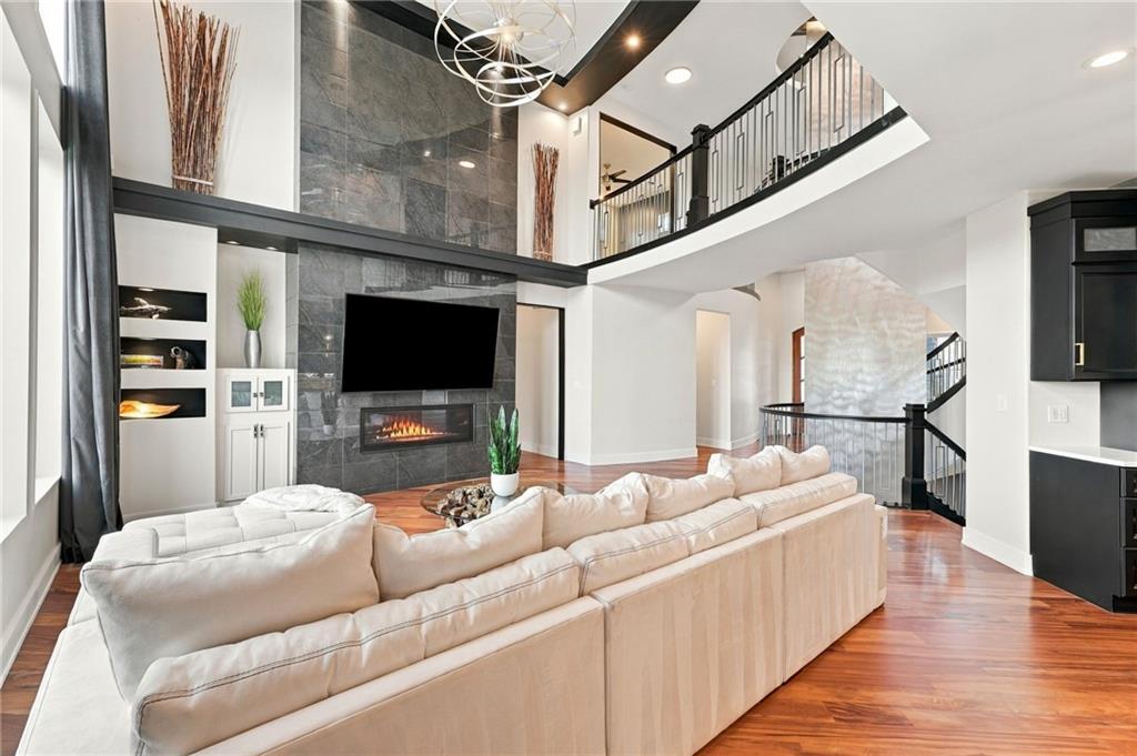 Two-story living room with a dark stone fireplace wall, cream sectional, and open staircase.