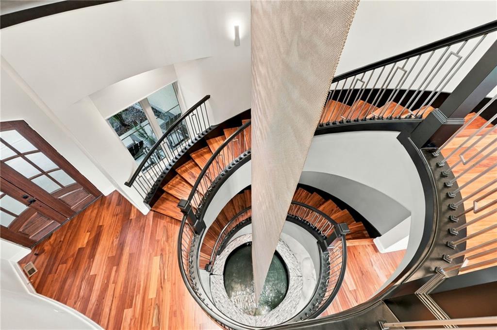 Curved wood staircase spirals around a circular water feature in a bright, multilevel interior.