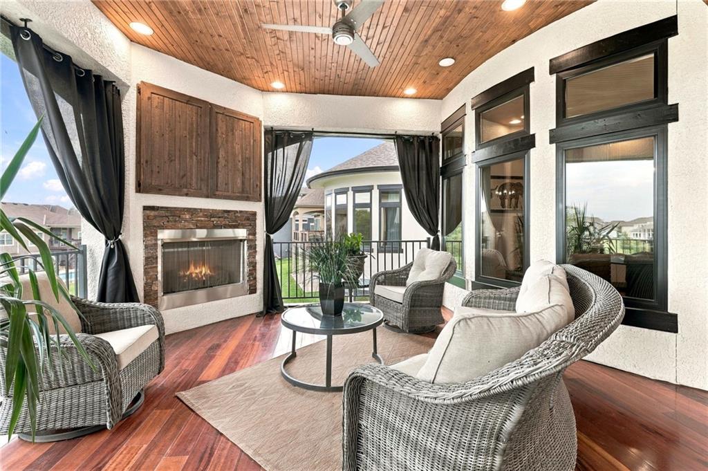 Covered sunroom with wicker seating, a wood-plank ceiling, and a stone fireplace