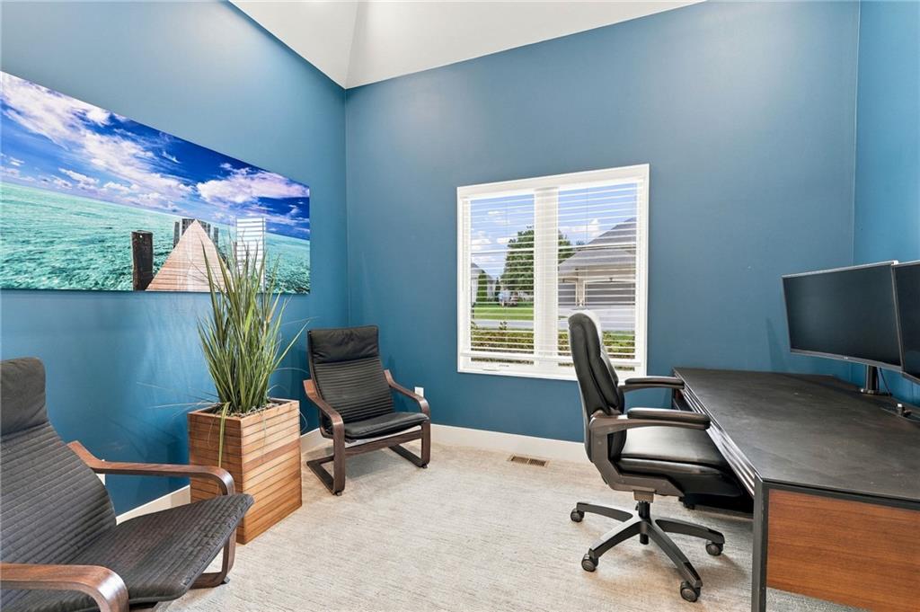 Home office with blue walls, a desk, black chairs, and large beach artwork.