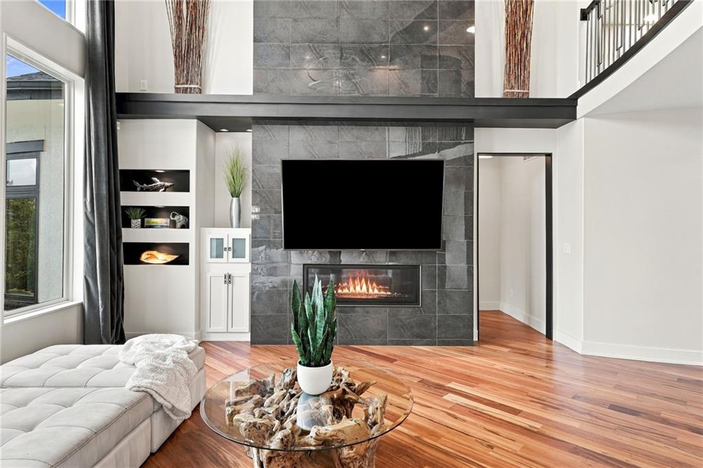 Two-story living room with a gray stone fireplace wall, mounted television, and warm hardwood floors.