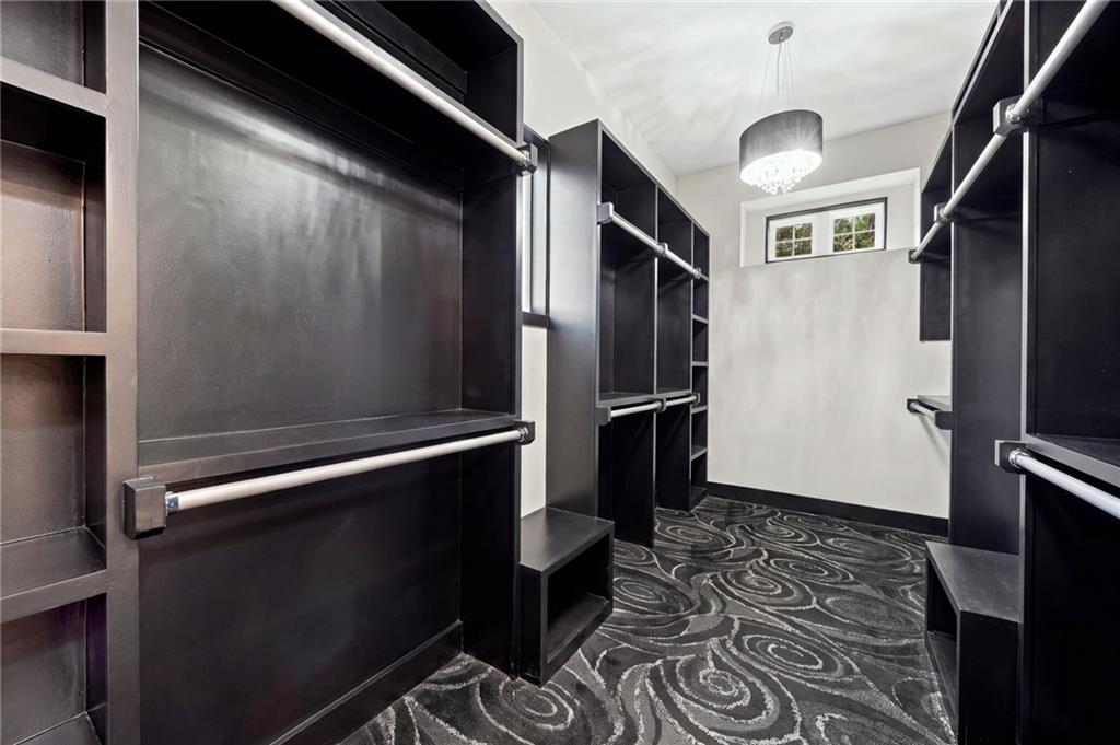 Walk-in closet with dark built-in cabinetry, patterned carpet, and a chandelier.