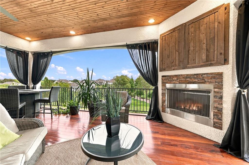 Covered patio with wicker seating, a wood ceiling, and a stone fireplace overlooking landscaped grounds.