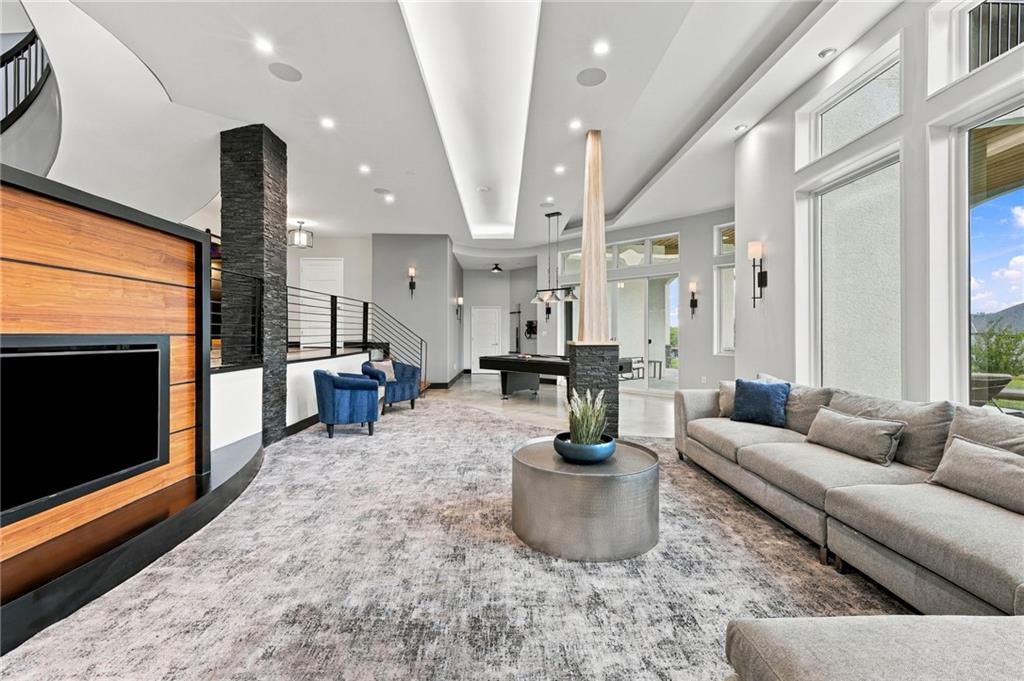 Open living room with tall windows, a wood-paneled TV wall, gray sectional, and pool table.