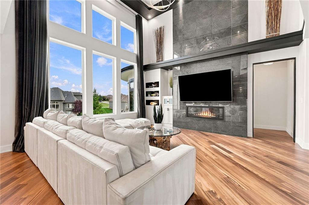 Double-height living room with tall windows, a white sectional, hardwood floors, and a stone fireplace wall.