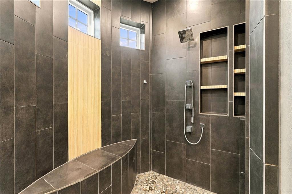 Walk-in shower with dark tile, pebble floor, built-in bench, and recessed shelves.
