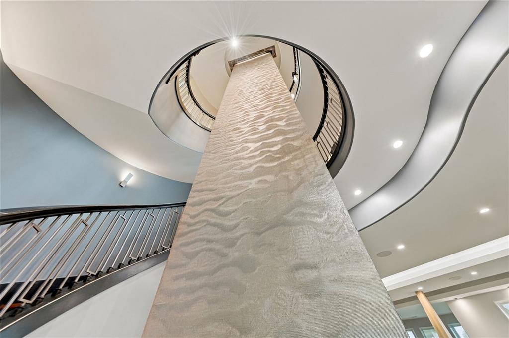 Curving staircase wraps around a tall textured stone column beneath a sculpted ceiling.