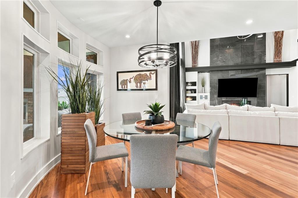 Dining area with a round glass table and gray chairs, opening onto a living room with a tiled fireplace.