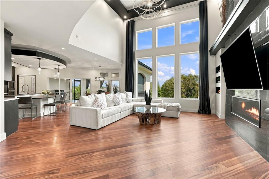 Living room with vaulted ceilings, tall windows, hardwood floors, and a fireplace beside a white sectional.