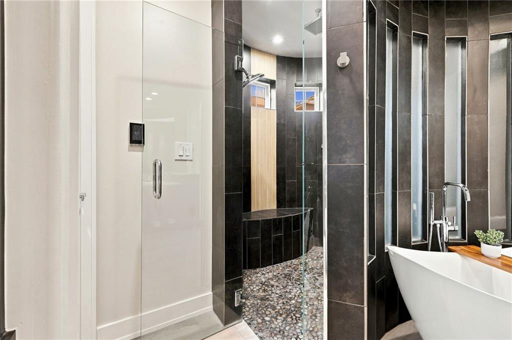 Modern bathroom with a pebble-floor walk-in shower and white freestanding tub.