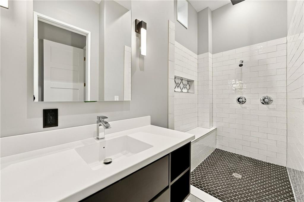 Bathroom with a white vanity and tiled walk-in shower with a dark hexagonal floor.