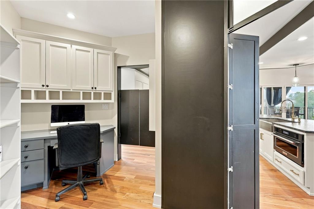 Home office nook with built-in white cabinets and desk, opening onto a bright kitchen.