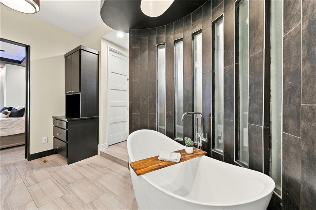 Bathroom with a freestanding soaking tub, wooden bath tray, and dark tiled accent wall.