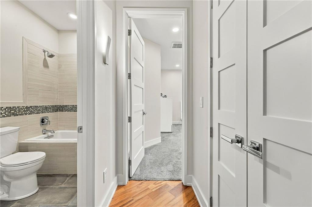Hallway with wood flooring beside an open bathroom with a tiled tub and toilet.