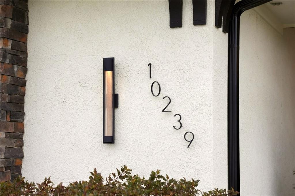 Home entry with diagonal black 10239 numbers on a white stucco wall beside a vertical light.