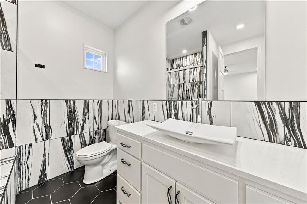 Bathroom with a white vessel sink and vanity, marble-pattern tile, and dark hexagonal floor.