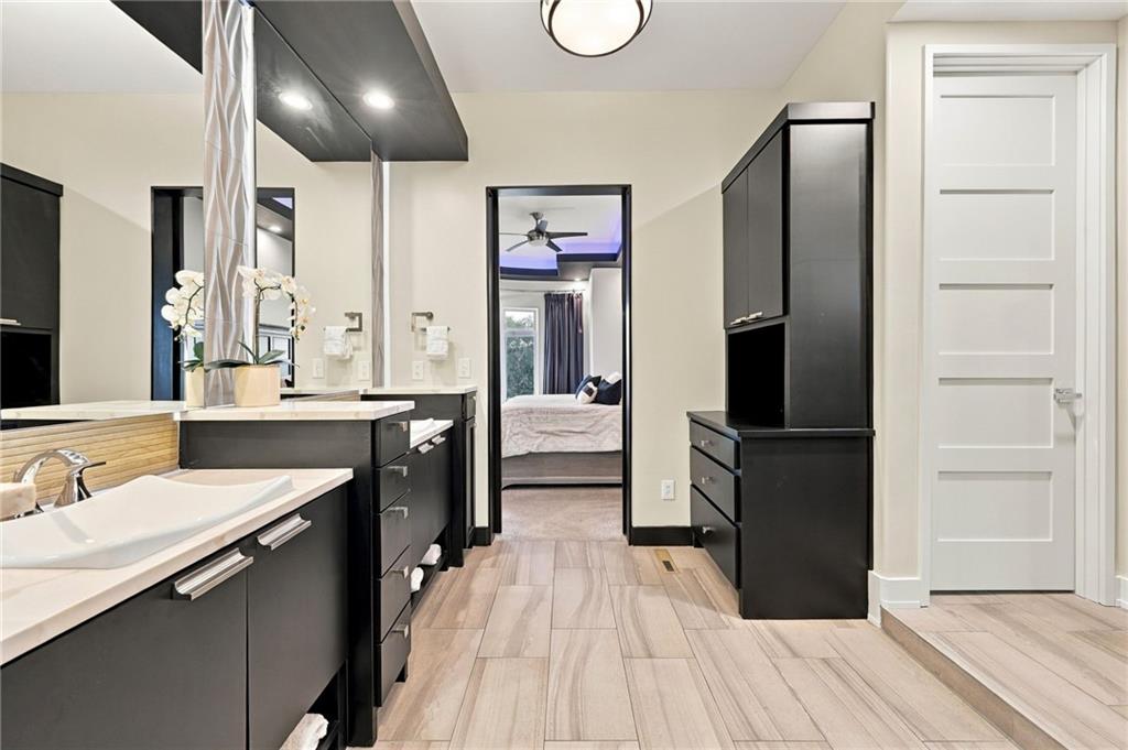 Bathroom with dark cabinetry, two vessel sinks, and a bedroom visible through the doorway.