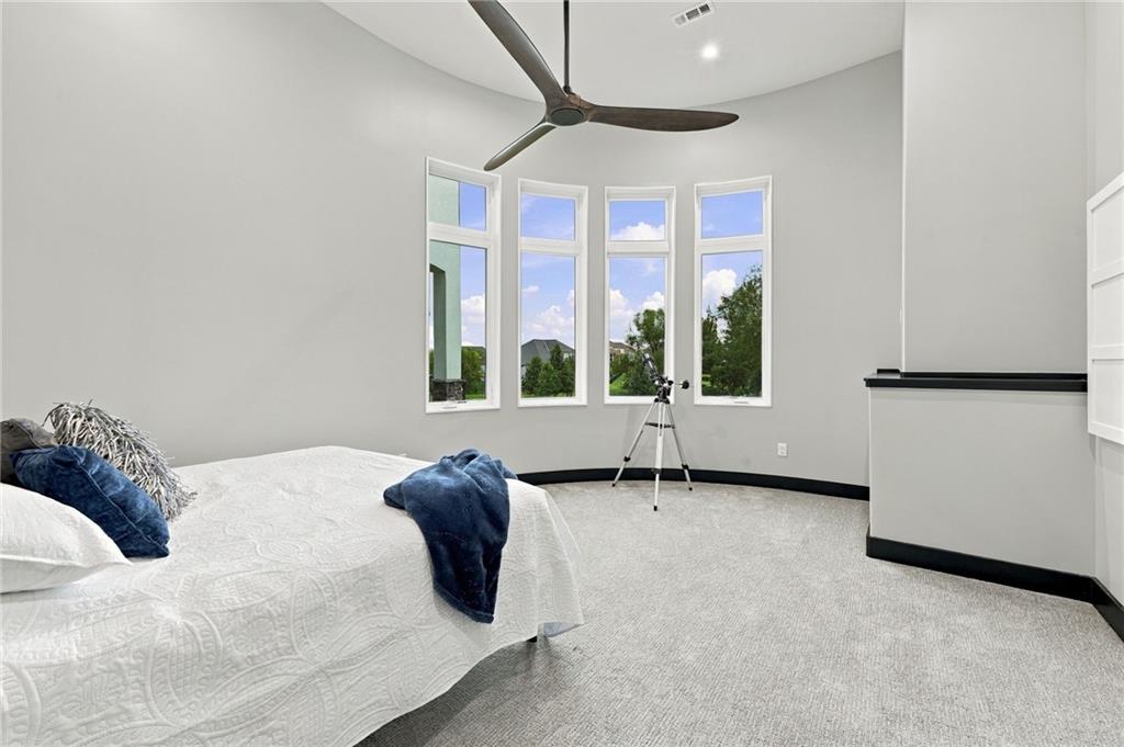 Bedroom with four tall windows, a ceiling fan, and a telescope beside the bed.