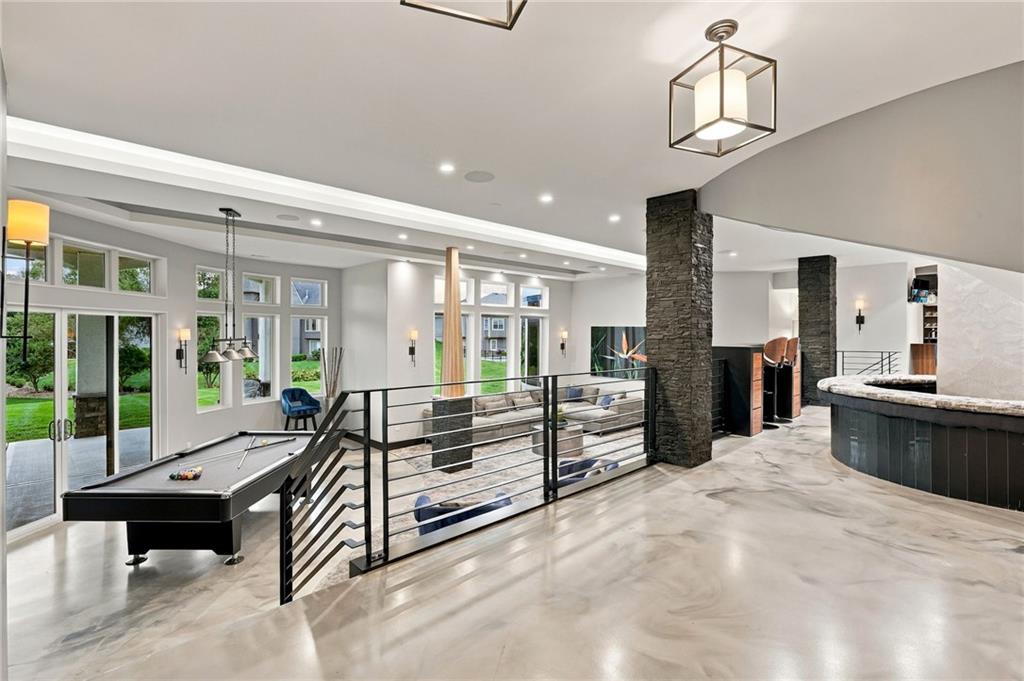 Open game room with a pool table, stone columns, and a railing overlooking the lower level.