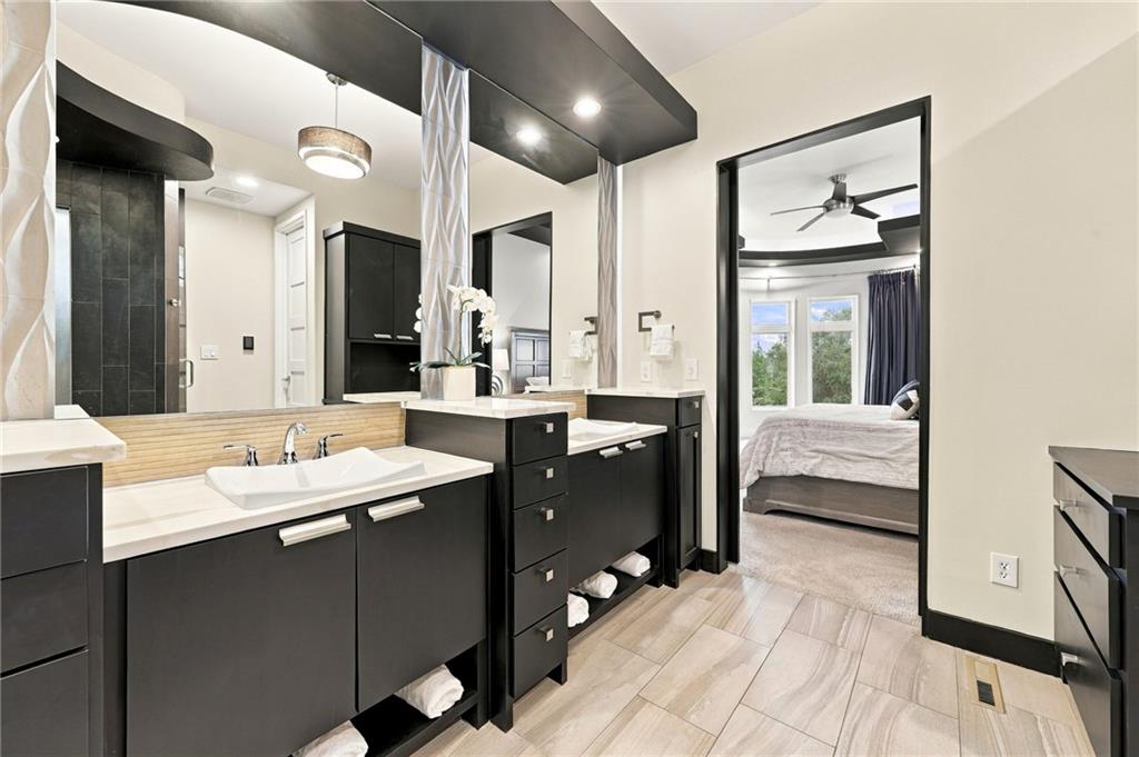 Primary bathroom with double black vanities and a dark tiled shower, opening to a bedroom.