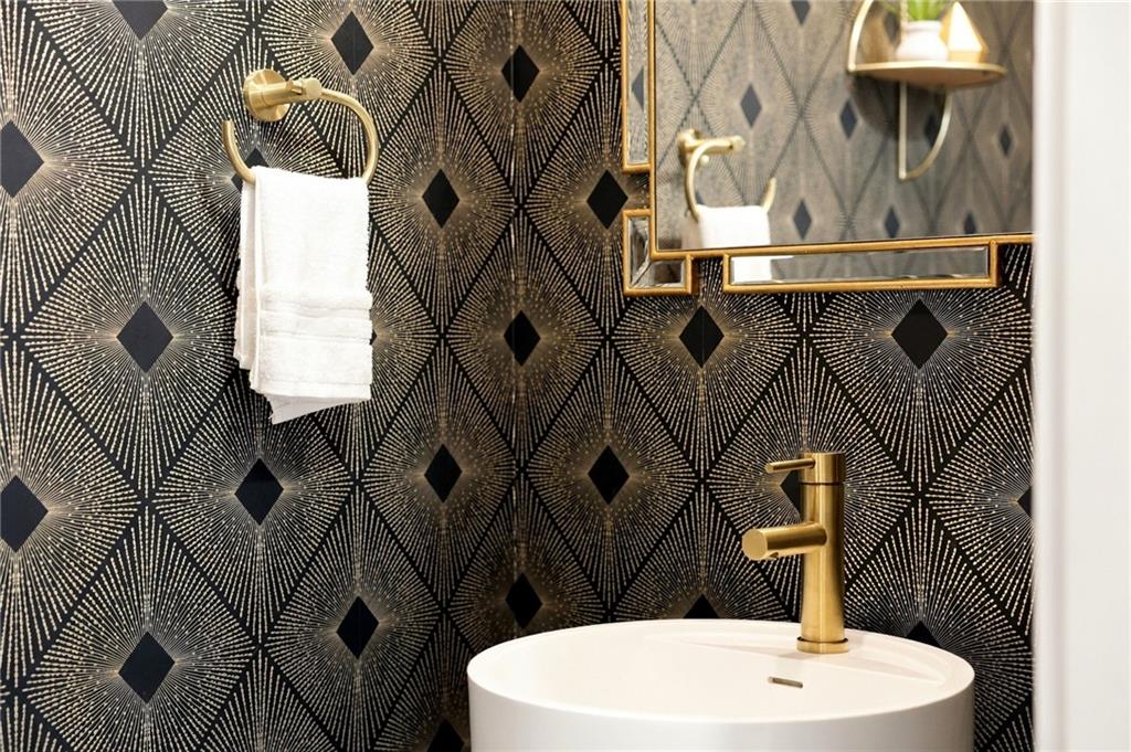 Bathroom vanity with a white vessel sink, gold fixtures, and bold black geometric tile.
