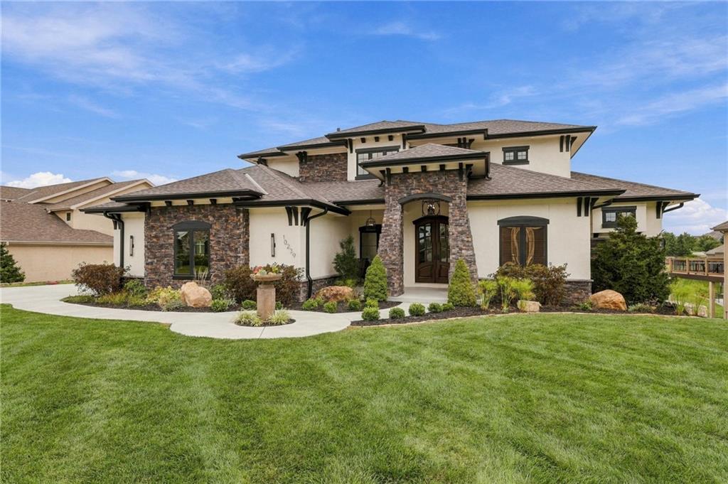 Two-story cream stucco home with stone accents, a covered entry, and a broad green lawn.
