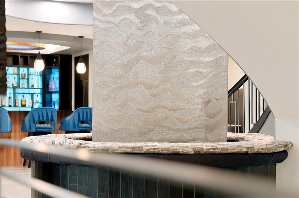 Stone fountain inside a home, with a curved staircase and blue lounge chairs near an illuminated bar.