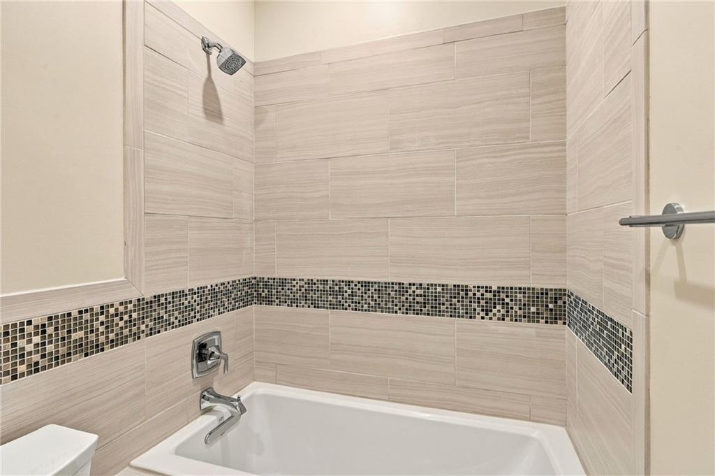 Bathroom tub and shower with beige tile, a dark mosaic accent band, and chrome fixtures.