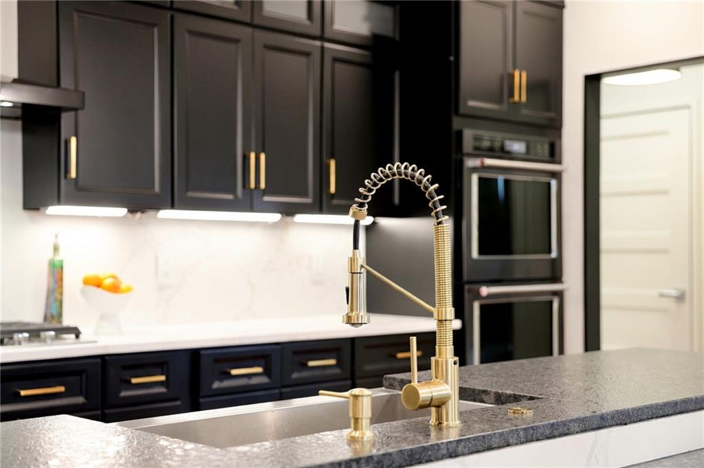 Modern kitchen with dark cabinets, a gray stone island, and a brass spring-coil faucet.