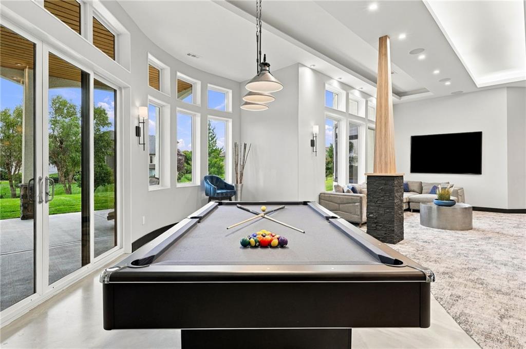Game room with a billiards table, tall windows, and a sitting area beside a stone-and-wood column.