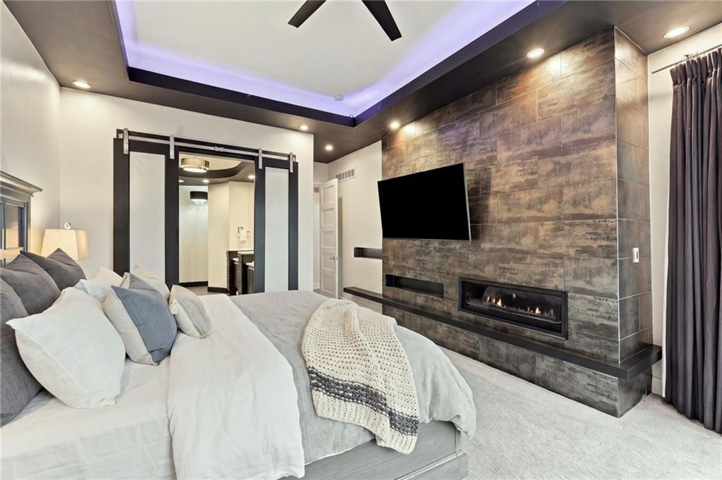 Bedroom with a stone feature wall, linear fireplace, mounted television, and tray ceiling.